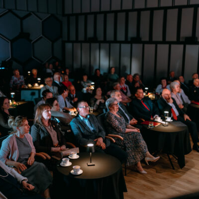 Goście i widownia zgromadzona w sali widowiskowej CKiS, siedząca przy okrągłych stolikach.